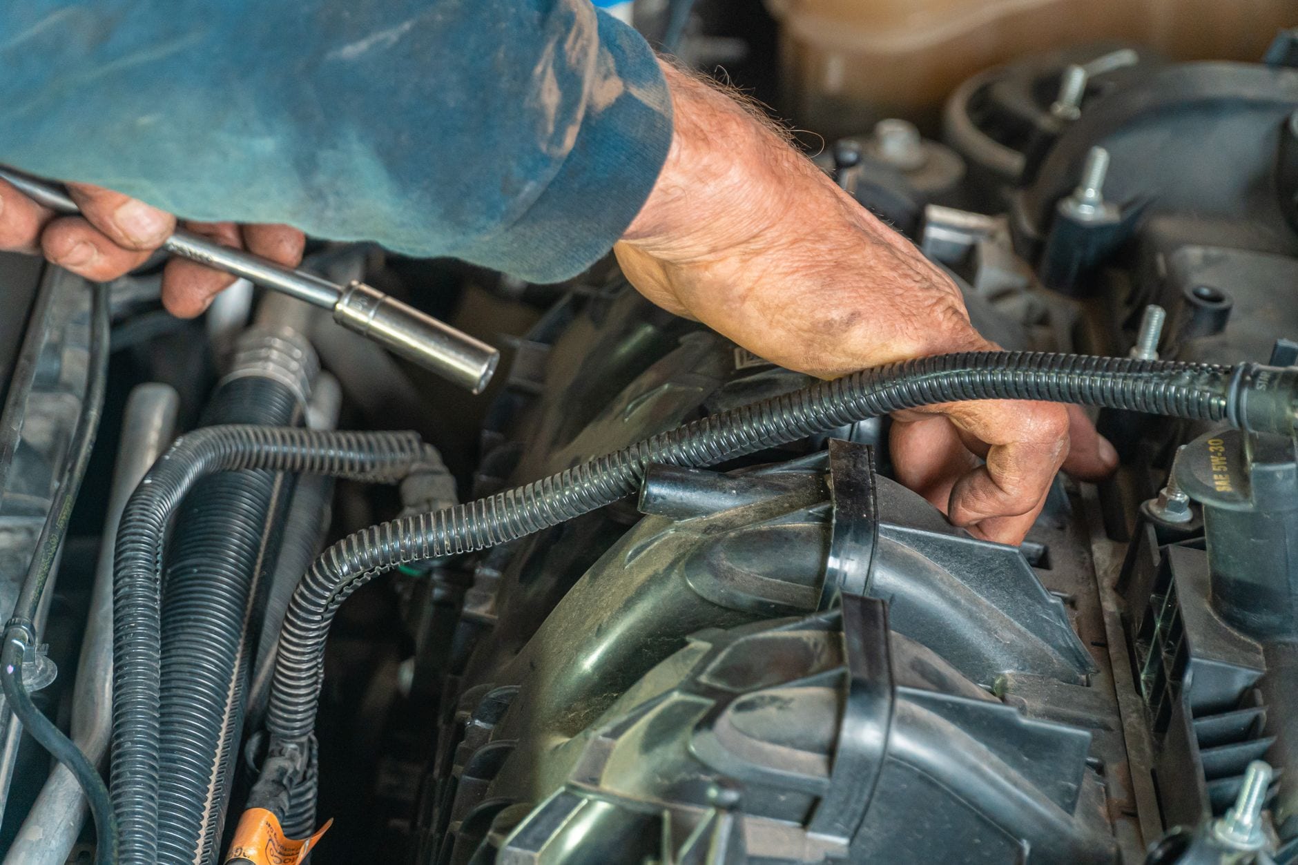 A mechanic's hands working on a car engine in an auto repair shop.